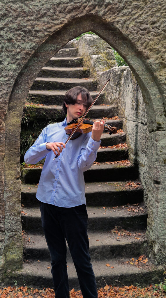 Der Musiker Johannes Rosenberg spielt die Geige. Er steht vor einer Stein-Treppe.
